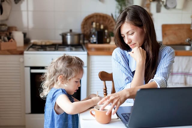 Working mom works from home office with kid. Woman and cute child using laptop.