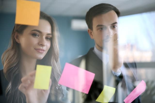 Man and woman placing sticky notes with ideas on glass