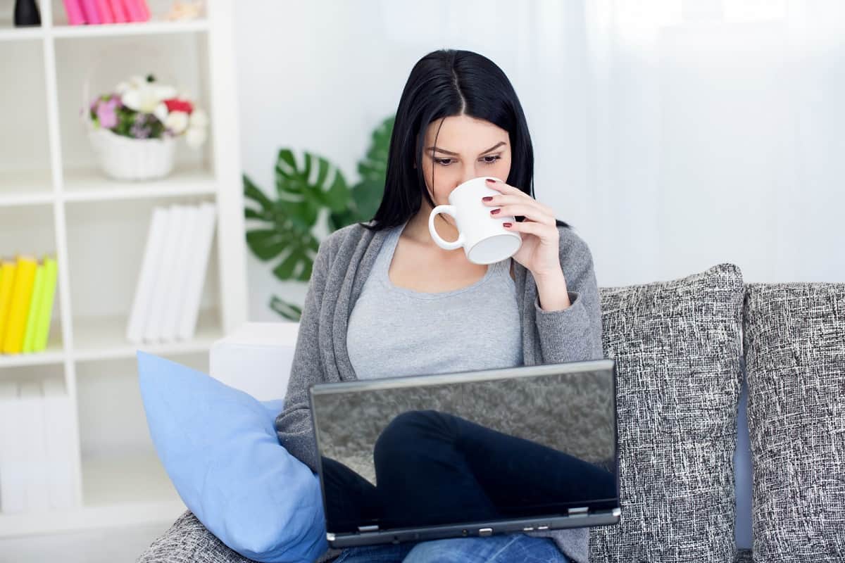 woman sipping coffee on a laptop while house sitting