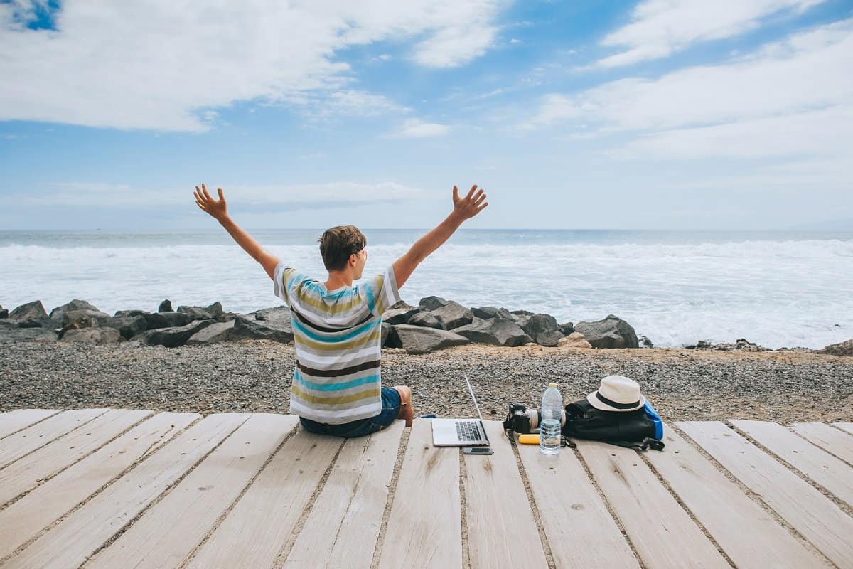 Photographer sitting outside with laptop and camera at the beach