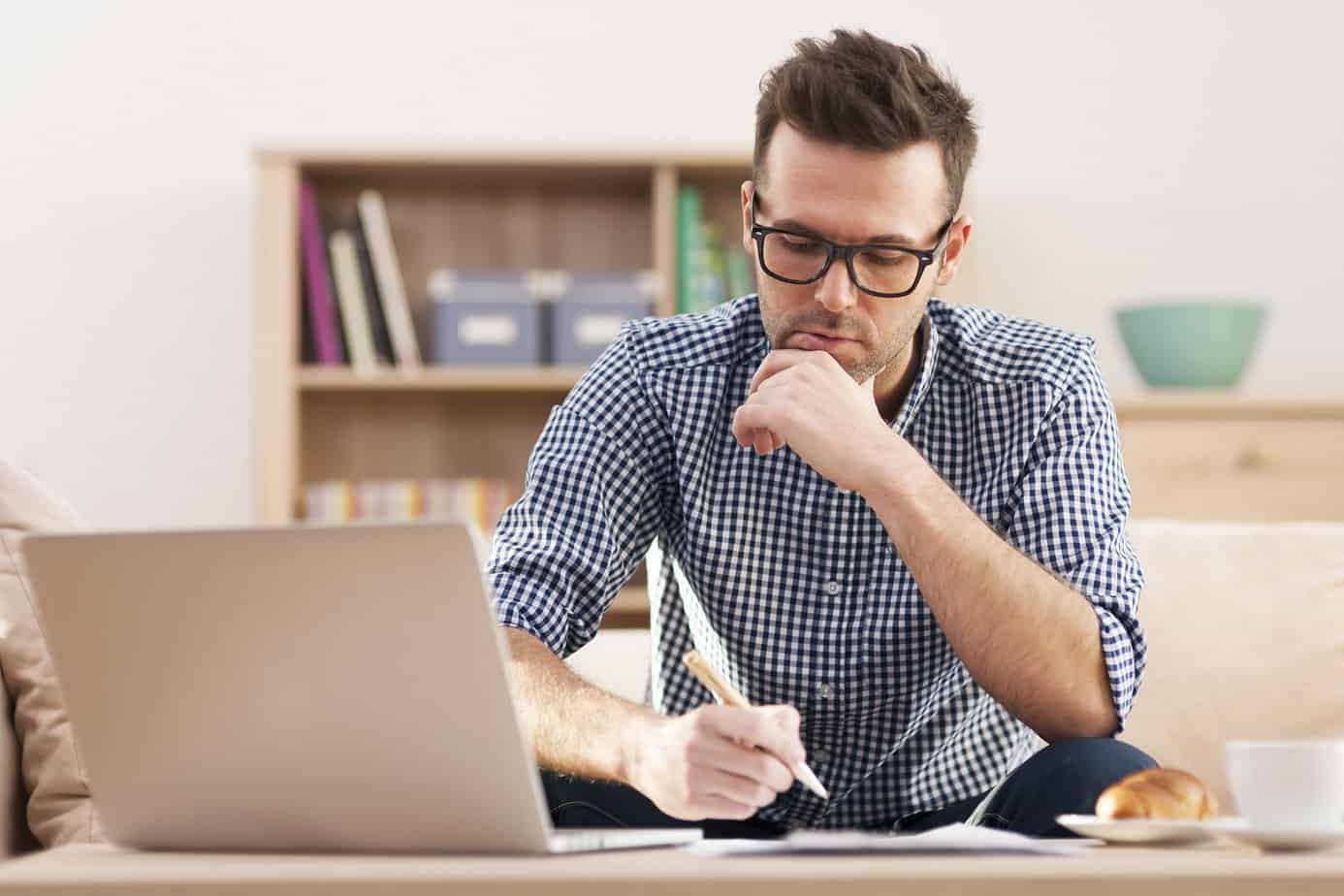 man writing notes in front of a laptop