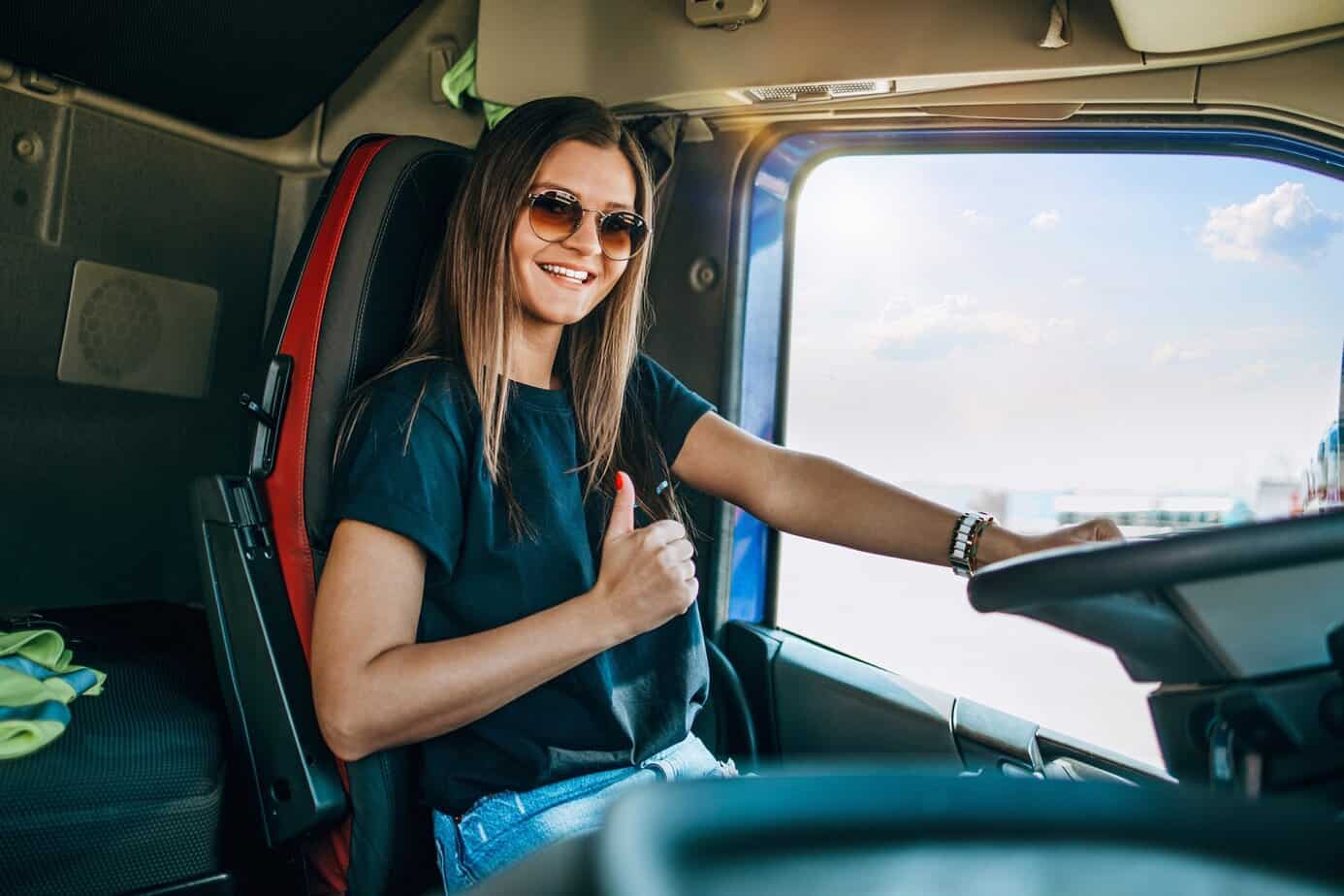 young woman giving thumbs up sign behind wheel of semi truck