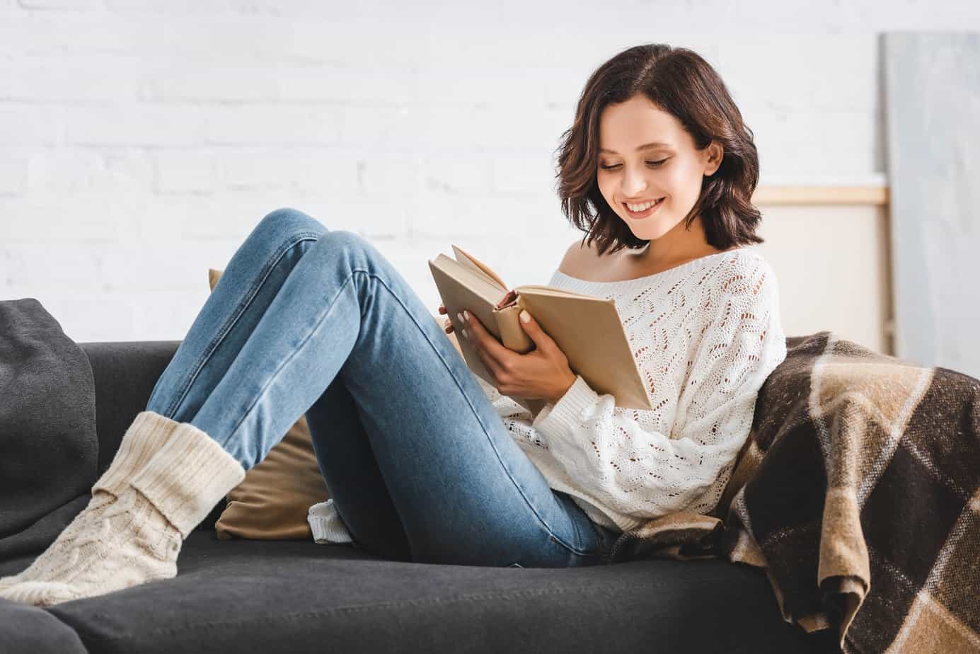 Woman smiling reading a book while lounging on a couch