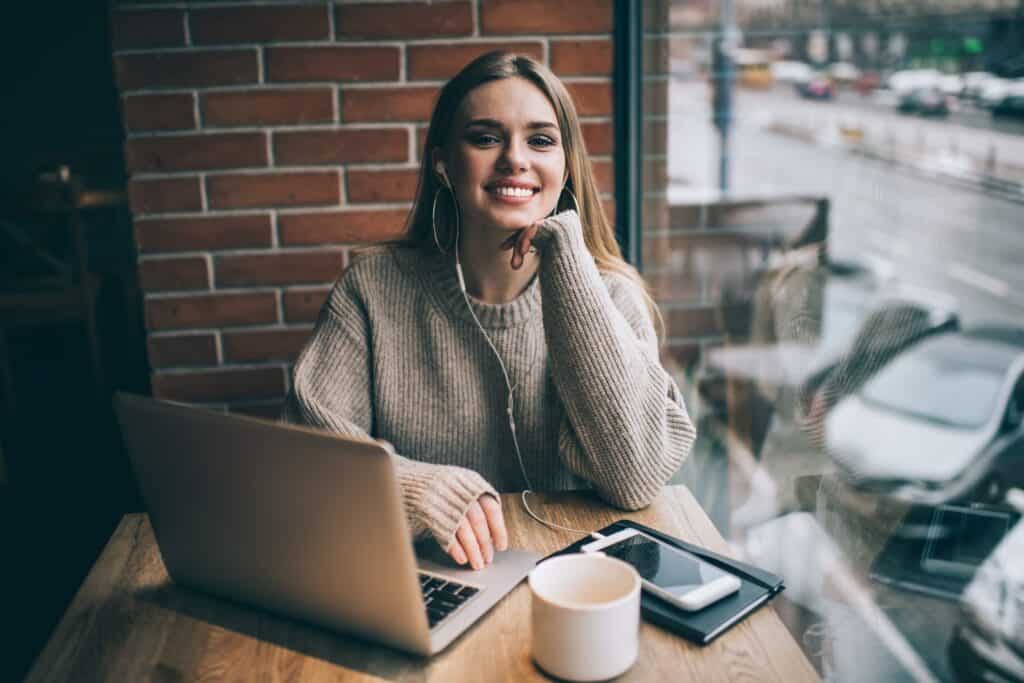 woman smiling in front of laptop next to large window