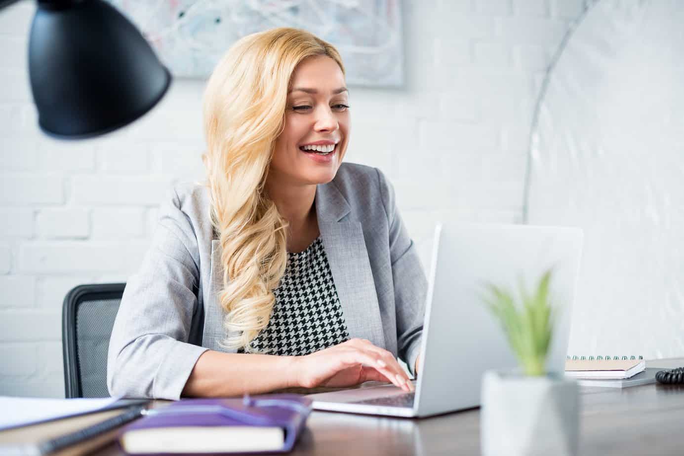 woman smiling while reviewing content on a laptop