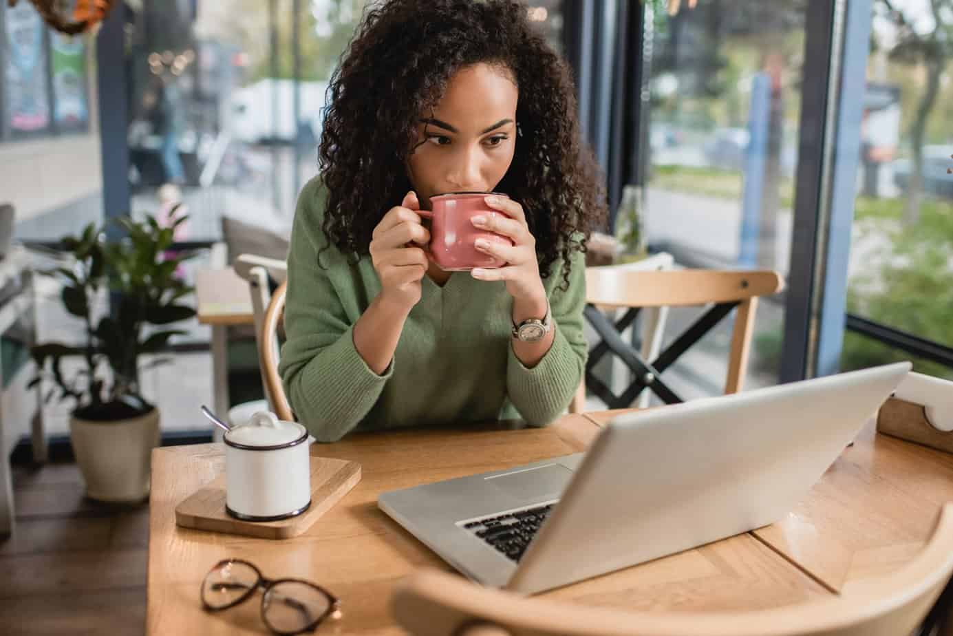 woman sipping from a mug looking at a laptop